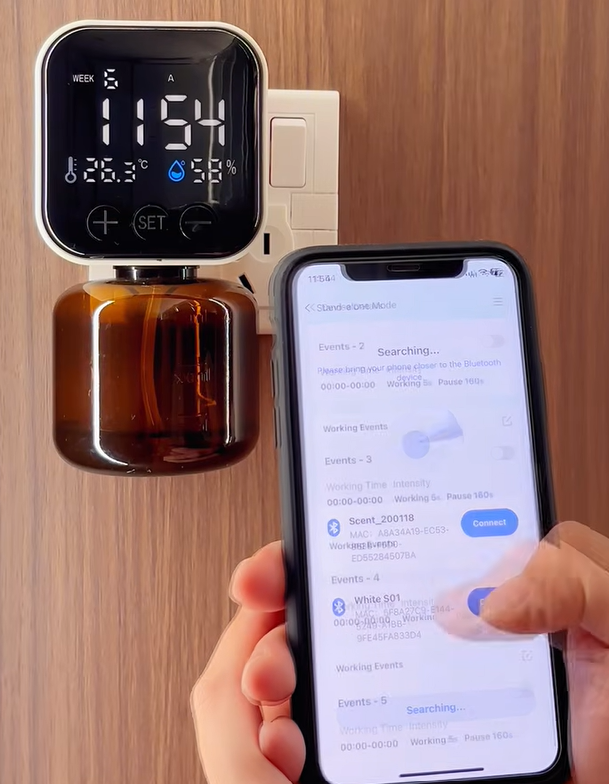 The Scentific Home diffuser plugged into a wall socket, paired with the AromaOS app on a phone